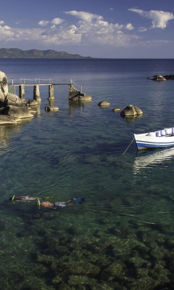 Scenic view of a clear lake with a boat and a swimmer near rocky shore.
