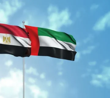 Egyptian and UAE flags waving against a blue sky.